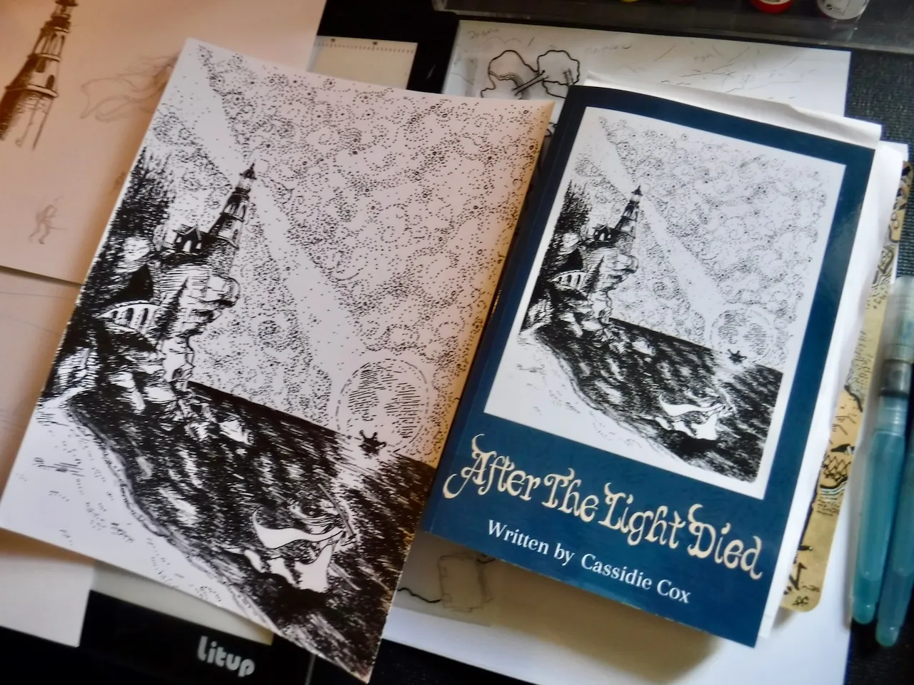 An illustrated book displayed beside its original ink artwork and an open sketchbook