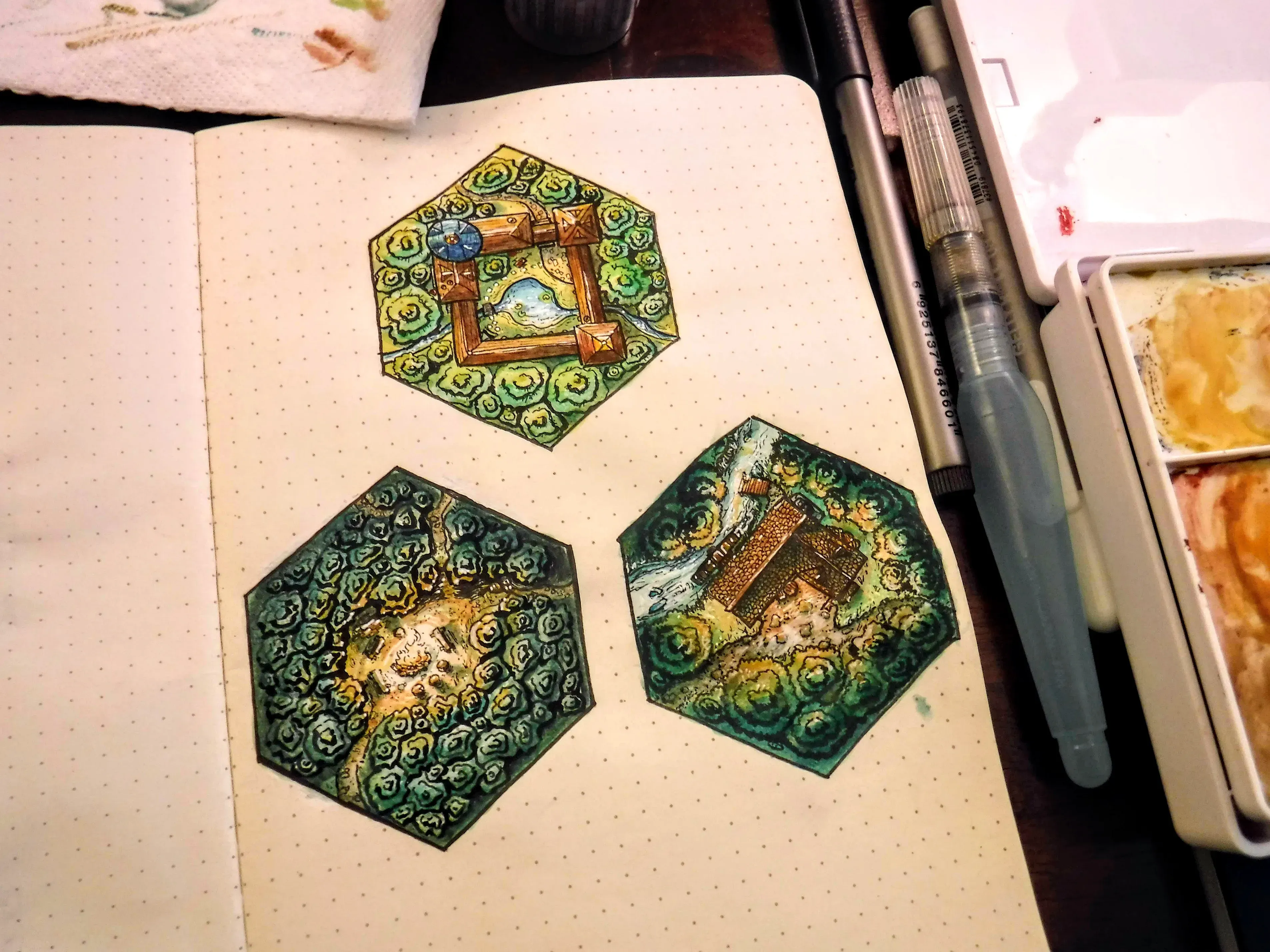 Three richly colored fantasy terrain hexes painted in an open sketchbook