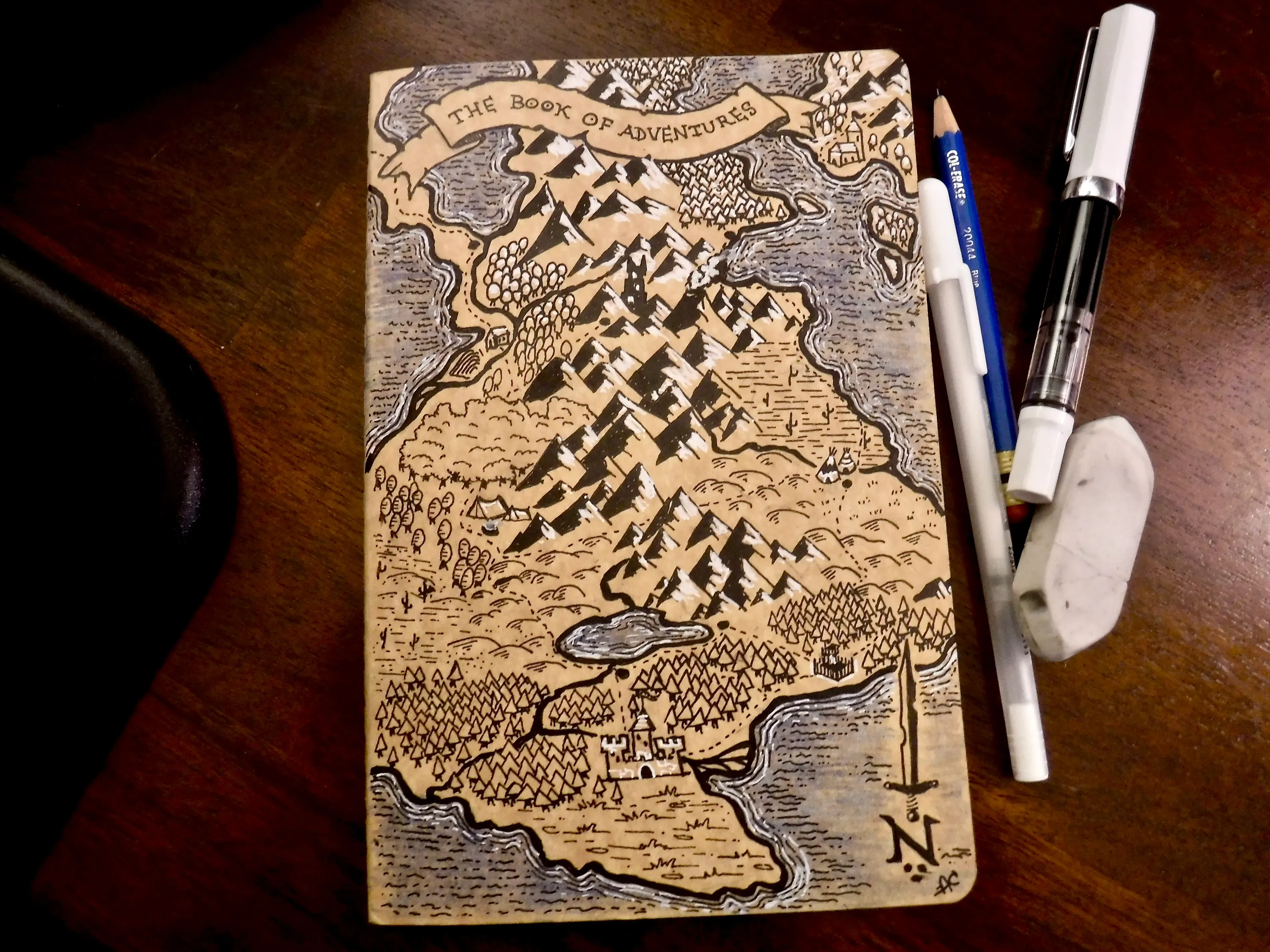 A hand-drawn adventure map covering a sketchbook beside drawing pens and pencils